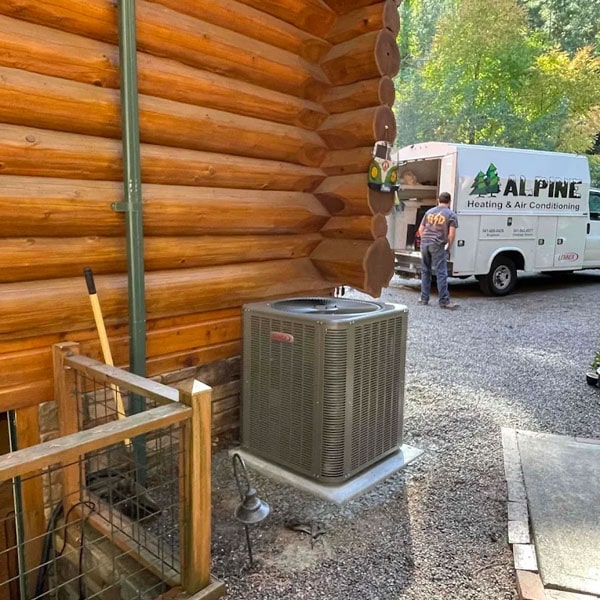Air conditioning unit outside a log cabin home with an Alpine work vehicle in the background.