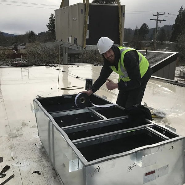 HVAC technician giving a thumbs up while installing an HVAC system on a rooftop.
