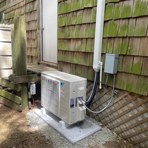 A Daikin heat pump outside a mossy older home.