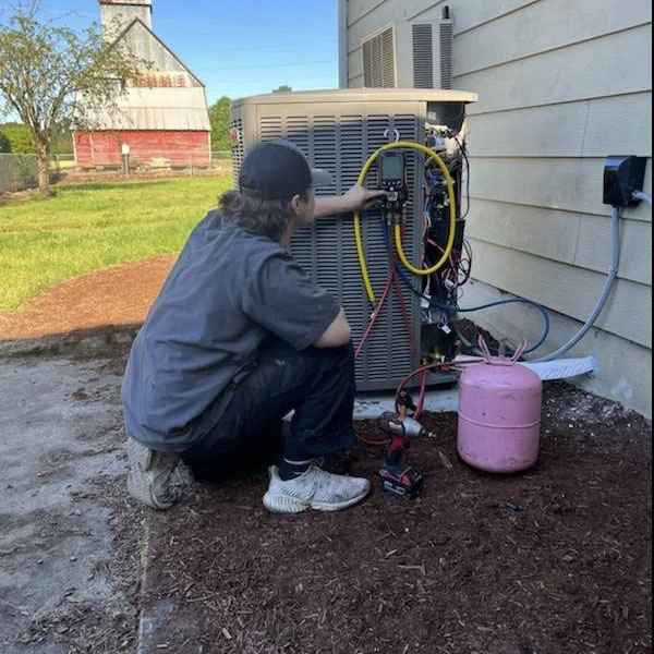 HVAC technician performing maintenance on a heat pump outside a home.