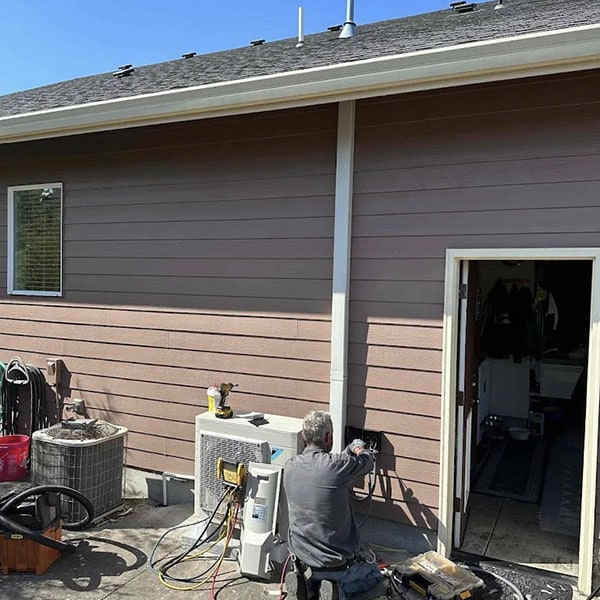 HVAC technician working on a heat pump and AC unit outside a home.