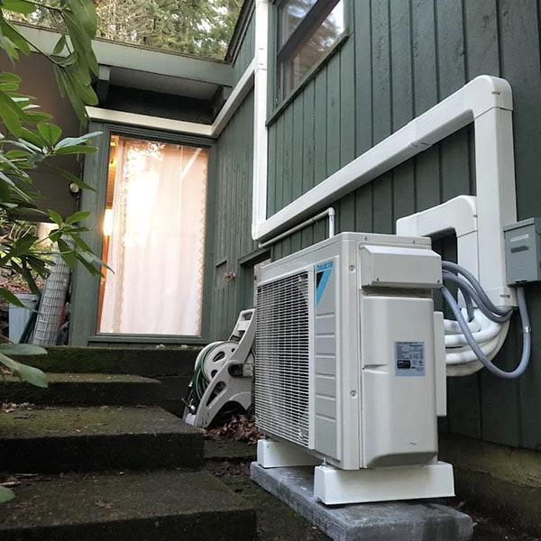A new Daikin heat pump installed outside a green colored home.