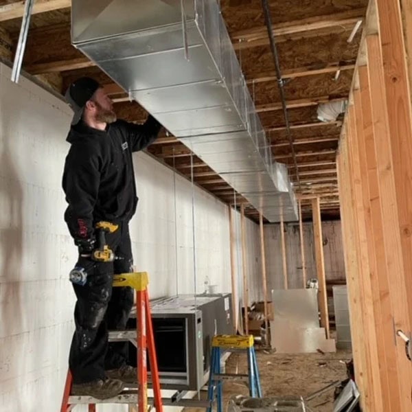 HVAC technician standing on a ladder checking the ducts of a home being built.