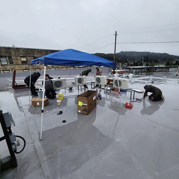 HVAC technicians working on a commercial rooftop on a rainy day.