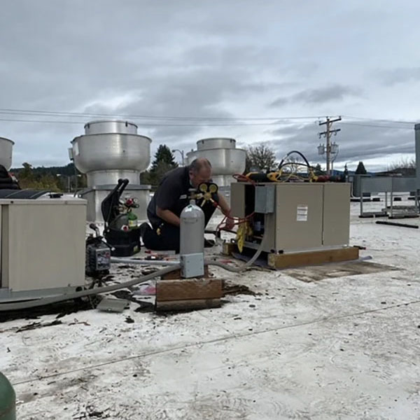 HVAC technician working on a commercial HVAC unit on a roof.