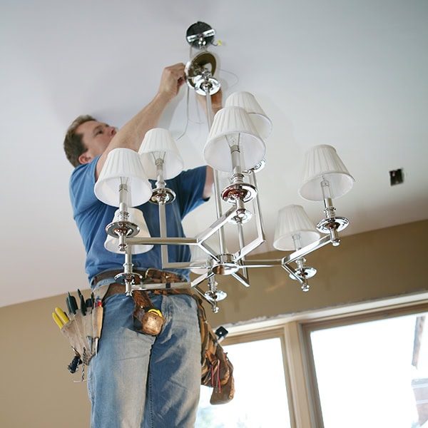 Electrical technician installing a light fixture in a home.