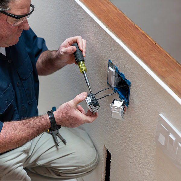 Electrical technician working on an electrical outlet in a home.
